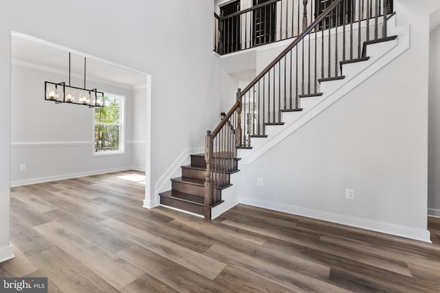 stairs with a high ceiling, ornamental molding, wood-type flooring, and a notable chandelier