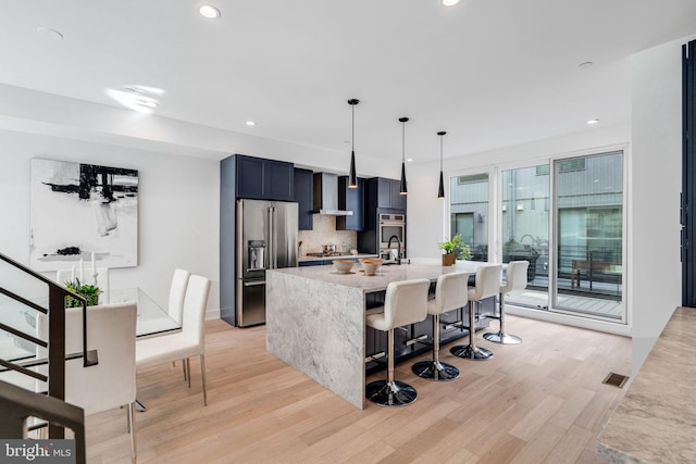 kitchen with a kitchen breakfast bar, hanging light fixtures, light hardwood / wood-style flooring, decorative backsplash, and appliances with stainless steel finishes