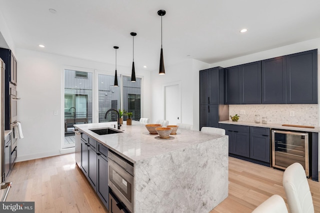 kitchen featuring light stone counters, sink, light hardwood / wood-style floors, wine cooler, and an island with sink