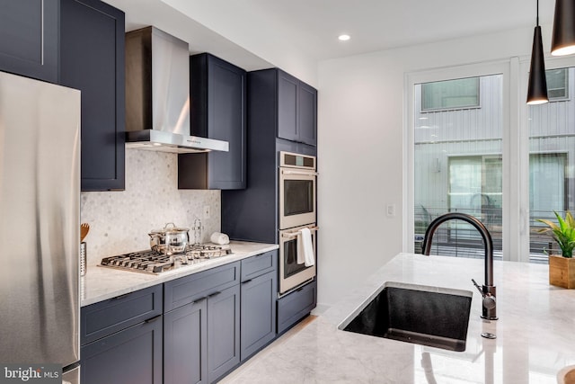 kitchen featuring light stone countertops, appliances with stainless steel finishes, wall chimney exhaust hood, sink, and pendant lighting