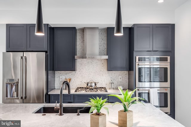 kitchen featuring backsplash, stainless steel appliances, sink, wall chimney range hood, and hanging light fixtures