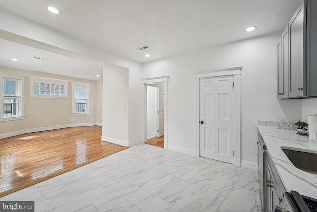 kitchen with light stone counters, gray cabinets, light hardwood / wood-style floors, and dishwasher