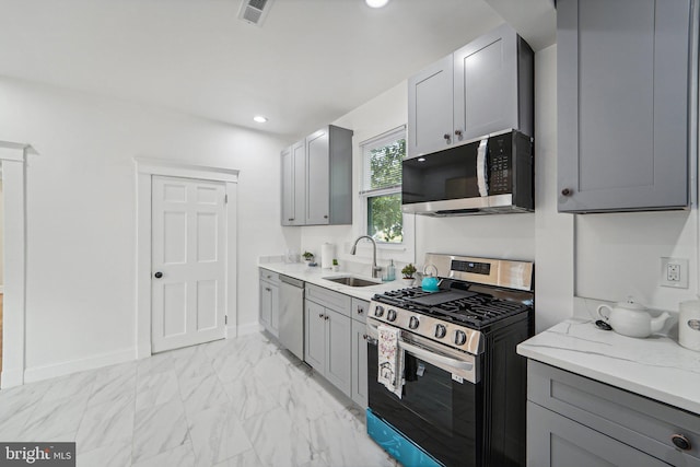 kitchen featuring gray cabinets, light stone countertops, appliances with stainless steel finishes, and sink