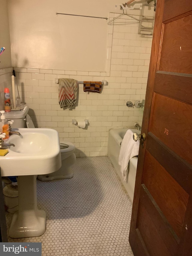 bathroom featuring a bathing tub, sink, tile patterned flooring, toilet, and tile walls