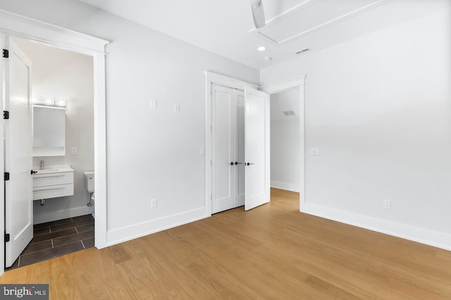 unfurnished bedroom featuring ensuite bathroom and hardwood / wood-style flooring