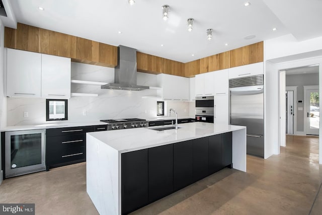 kitchen featuring exhaust hood, a center island with sink, white cabinetry, stainless steel appliances, and beverage cooler