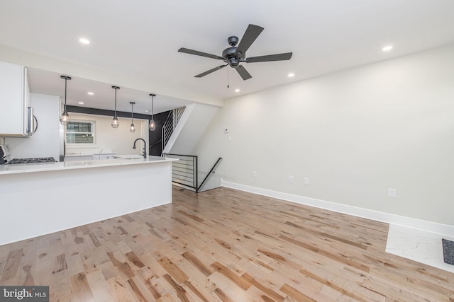 kitchen featuring stove, sink, light hardwood / wood-style floors, white cabinetry, and hanging light fixtures