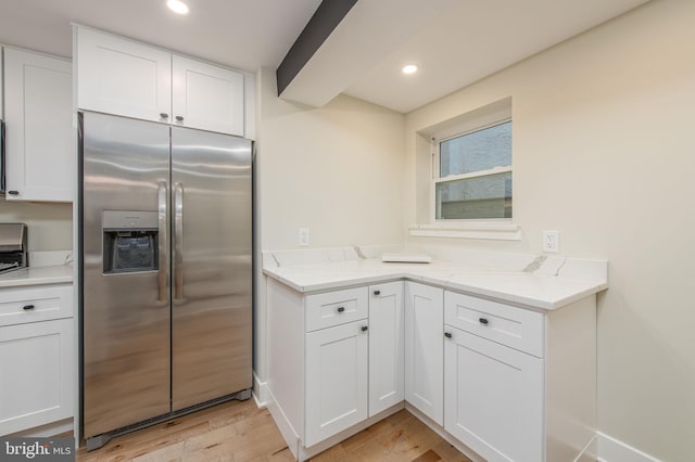 kitchen with light hardwood / wood-style floors, white cabinetry, light stone counters, and stainless steel fridge with ice dispenser