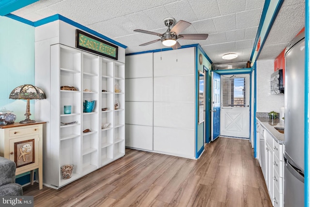 kitchen with white cabinets, ceiling fan, stainless steel fridge, and light hardwood / wood-style flooring