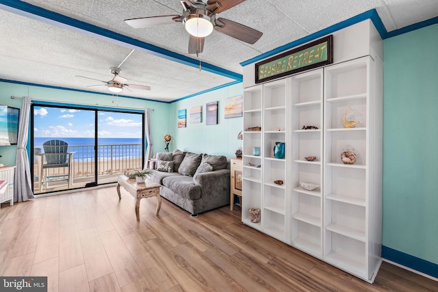 living area featuring ornamental molding, a textured ceiling, a water view, and light hardwood / wood-style floors