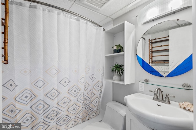 bathroom featuring a paneled ceiling, toilet, sink, and a shower with shower curtain