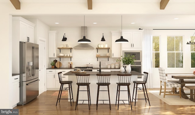 kitchen featuring stainless steel appliances, hardwood / wood-style floors, white cabinetry, hanging light fixtures, and an island with sink