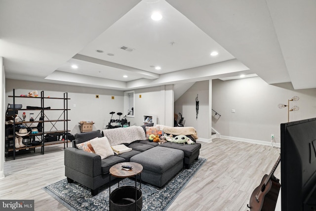 living room with a raised ceiling and light wood-type flooring