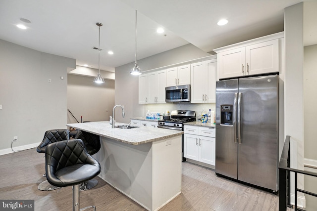 kitchen featuring pendant lighting, white cabinetry, sink, stainless steel appliances, and a center island with sink