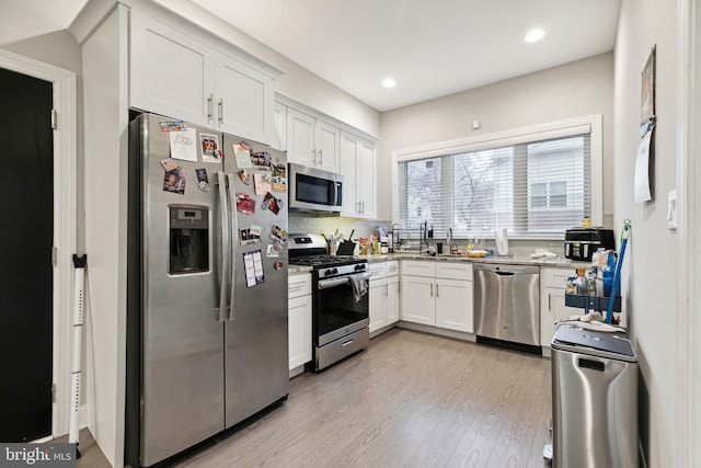 kitchen with sink, appliances with stainless steel finishes, white cabinets, light hardwood / wood-style floors, and backsplash