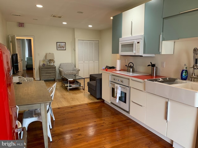 kitchen featuring black electric cooktop, sink, white cabinetry, hardwood / wood-style floors, and oven