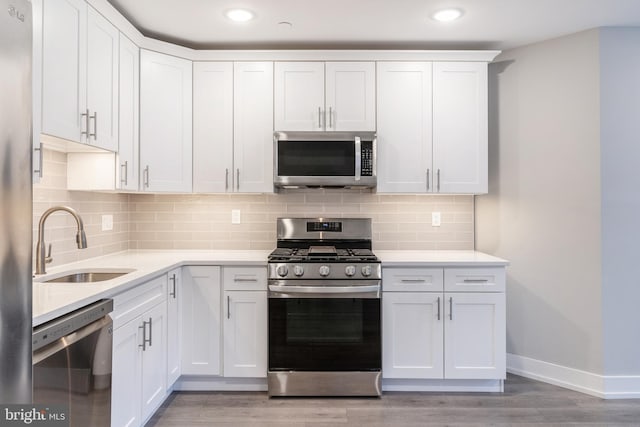 kitchen with sink, light hardwood / wood-style floors, decorative backsplash, white cabinets, and appliances with stainless steel finishes