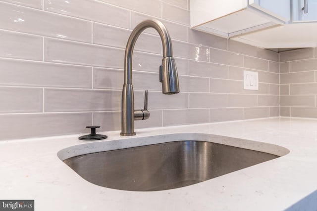 details featuring backsplash, light stone countertops, and sink