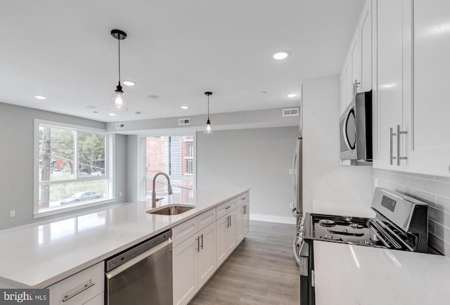 kitchen featuring stainless steel appliances, sink, pendant lighting, light hardwood / wood-style flooring, and white cabinetry