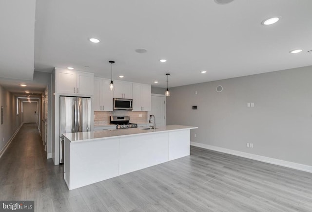 kitchen featuring white cabinetry, hanging light fixtures, stainless steel appliances, light hardwood / wood-style floors, and a center island with sink