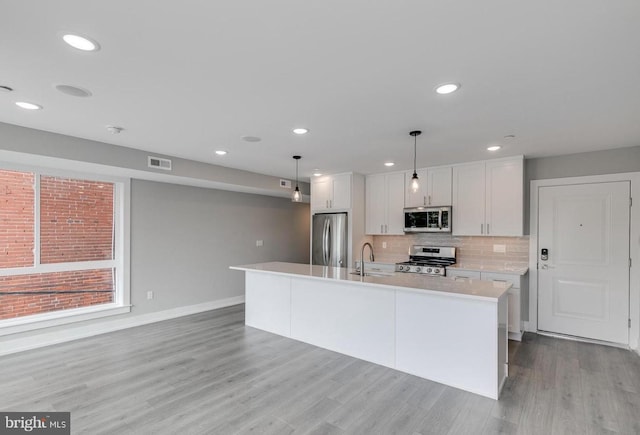 kitchen featuring pendant lighting, a center island with sink, light hardwood / wood-style flooring, white cabinetry, and stainless steel appliances