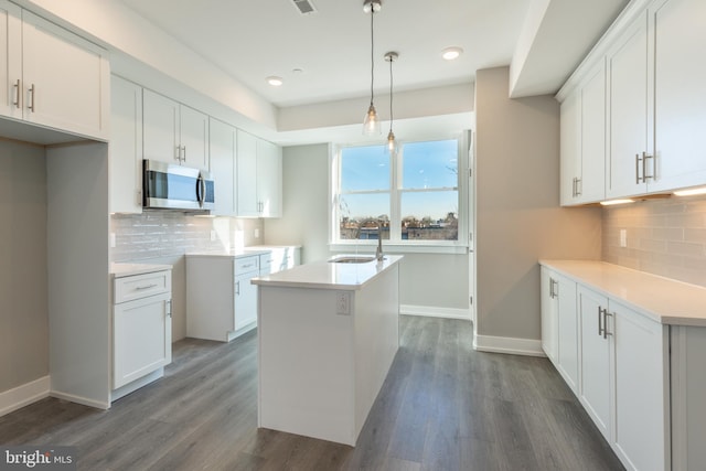 kitchen with dark hardwood / wood-style flooring, a kitchen island with sink, sink, pendant lighting, and white cabinetry