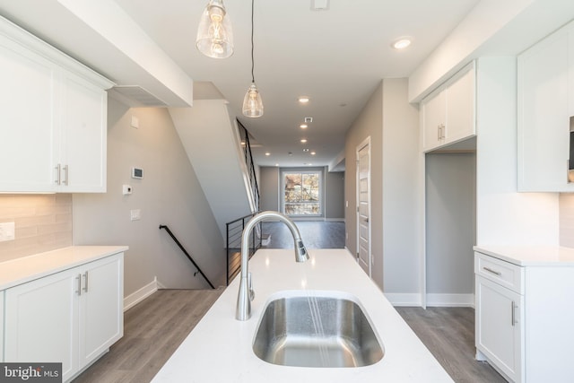 kitchen featuring dark wood-type flooring, sink, white cabinets, and hanging light fixtures