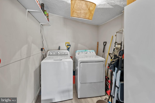 clothes washing area with a textured ceiling, washing machine and dryer, and light hardwood / wood-style flooring