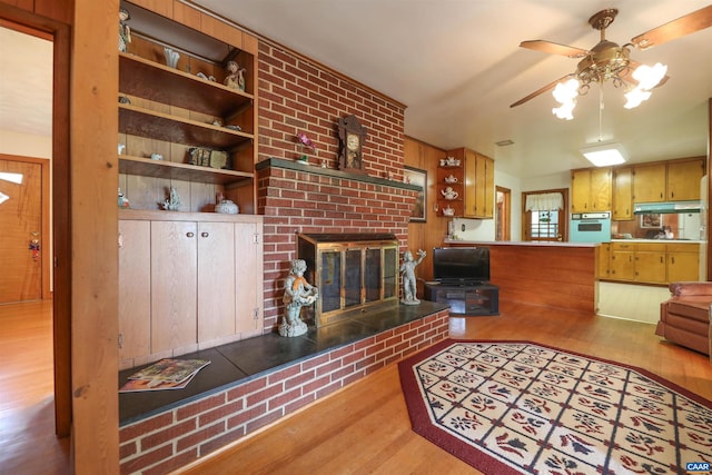 living room with light wood-type flooring, ceiling fan, a brick fireplace, and built in shelves