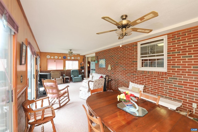 carpeted dining room featuring brick wall, a healthy amount of sunlight, ornamental molding, and wood walls