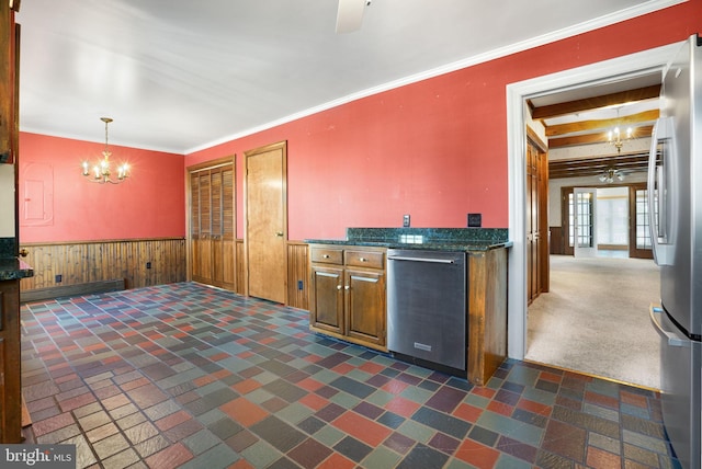 kitchen with stainless steel appliances, hanging light fixtures, wood walls, dark carpet, and ornamental molding