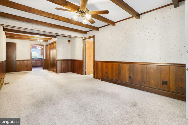 carpeted spare room with wood walls, beamed ceiling, and ceiling fan