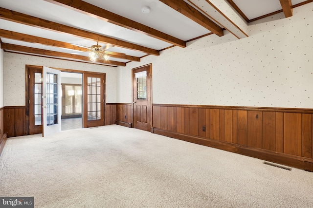 spare room featuring carpet, french doors, wooden walls, ceiling fan, and beamed ceiling