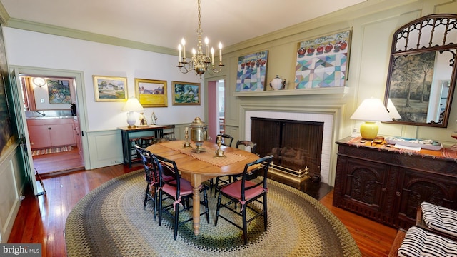 dining space featuring a brick fireplace, a chandelier, ornamental molding, and hardwood / wood-style flooring