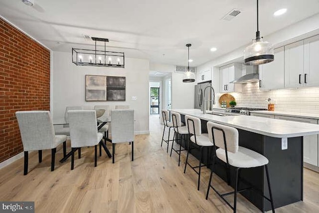 kitchen featuring white cabinets, hanging light fixtures, brick wall, and an island with sink