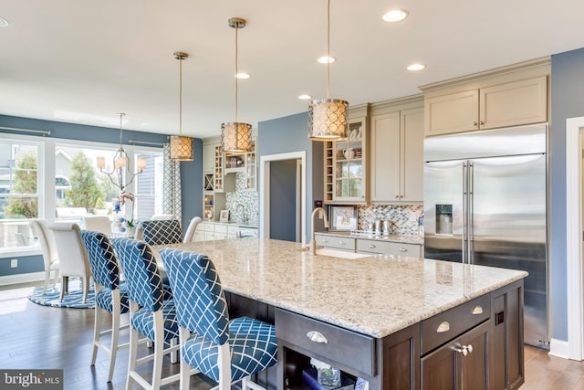 kitchen featuring cream cabinetry, a center island with sink, tasteful backsplash, built in fridge, and hanging light fixtures