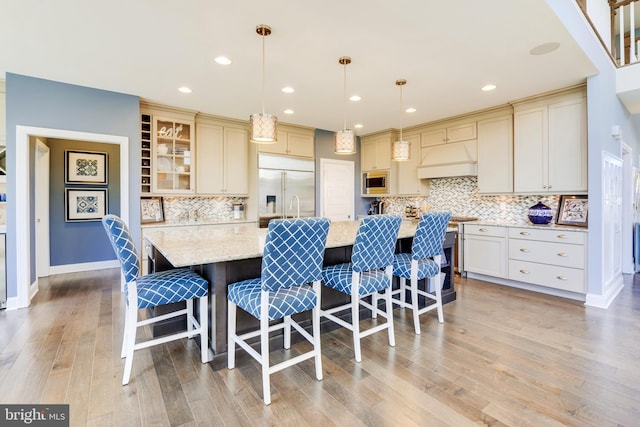 kitchen featuring premium range hood, decorative backsplash, decorative light fixtures, a kitchen island with sink, and built in appliances