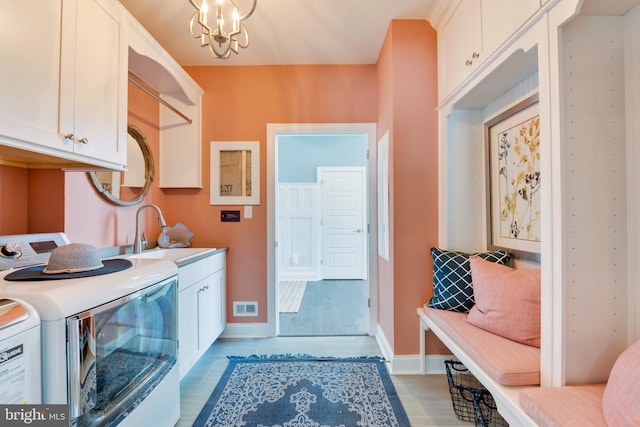 laundry area with light hardwood / wood-style floors, washer and dryer, a notable chandelier, cabinets, and sink