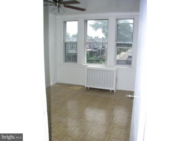 unfurnished room featuring radiator heating unit, dark parquet floors, plenty of natural light, and ceiling fan