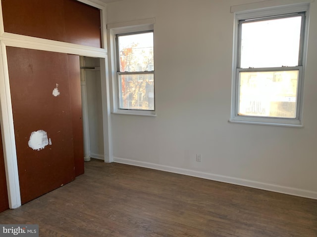 unfurnished bedroom with a closet, multiple windows, and dark wood-type flooring