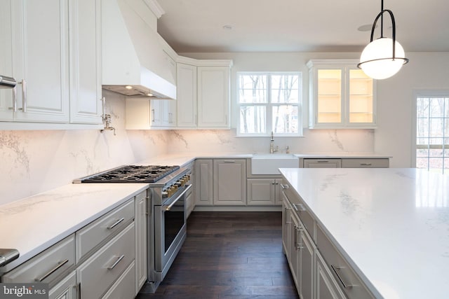 kitchen with high end range, sink, custom range hood, decorative light fixtures, and white cabinetry