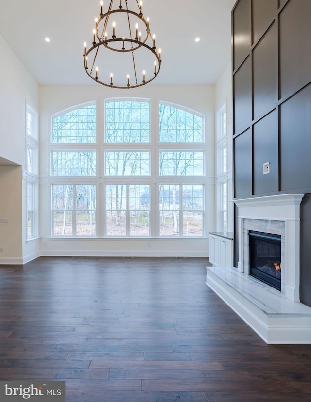 unfurnished living room featuring a high end fireplace, an inviting chandelier, a wealth of natural light, and dark wood-type flooring