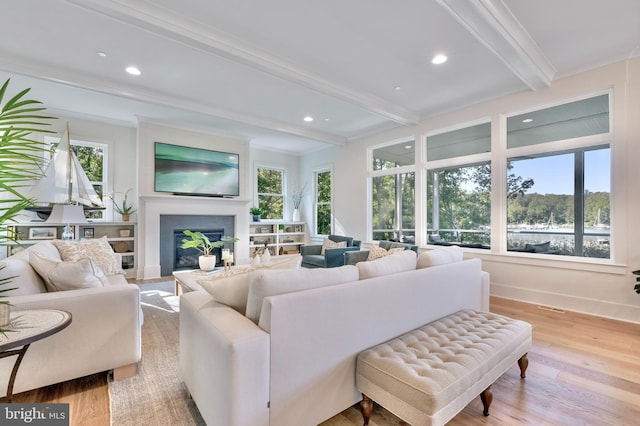 living room with ornamental molding, beamed ceiling, light hardwood / wood-style floors, and a wealth of natural light