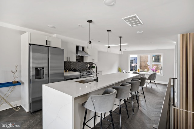 kitchen with hanging light fixtures, wall chimney range hood, stainless steel fridge with ice dispenser, a center island with sink, and white cabinets