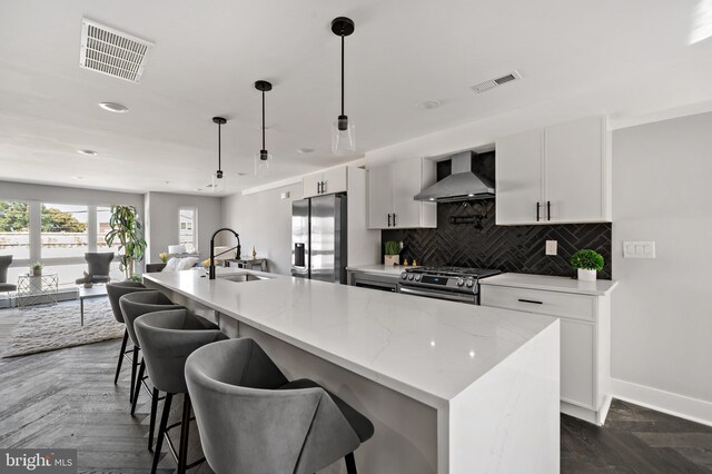 kitchen with appliances with stainless steel finishes, dark parquet flooring, sink, wall chimney range hood, and a center island with sink