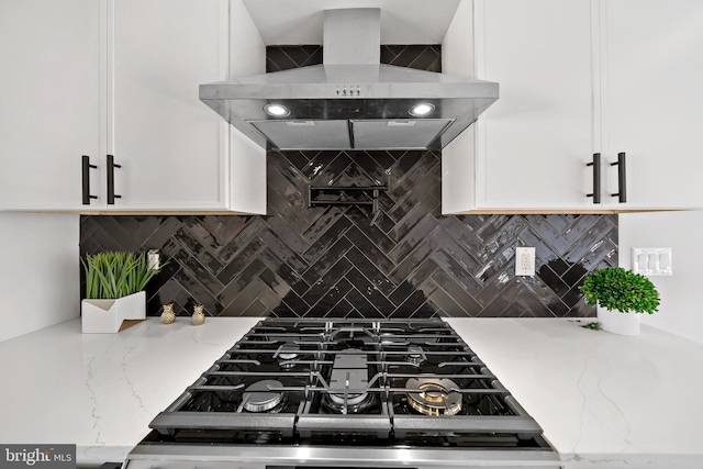 kitchen with white cabinetry, backsplash, light stone counters, and wall chimney range hood