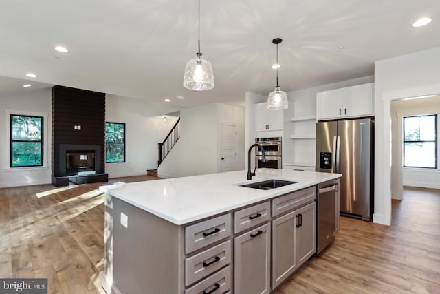 kitchen featuring appliances with stainless steel finishes, gray cabinetry, a kitchen island with sink, decorative light fixtures, and a fireplace