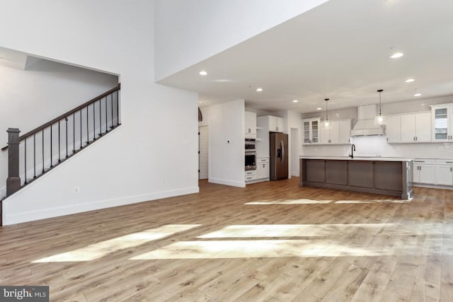 kitchen featuring appliances with stainless steel finishes, light wood-type flooring, decorative light fixtures, white cabinets, and an island with sink