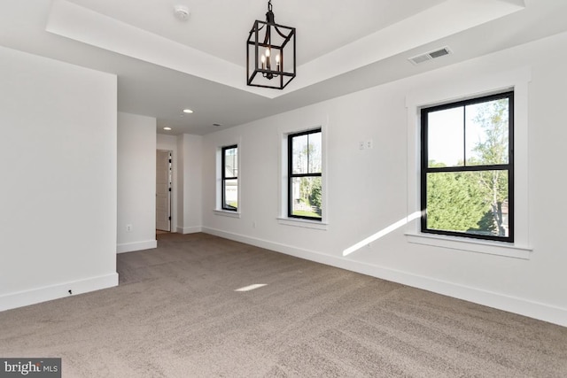 spare room featuring carpet, a tray ceiling, and an inviting chandelier