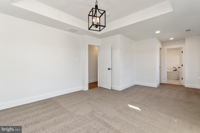 unfurnished room with a raised ceiling, carpet floors, and an inviting chandelier